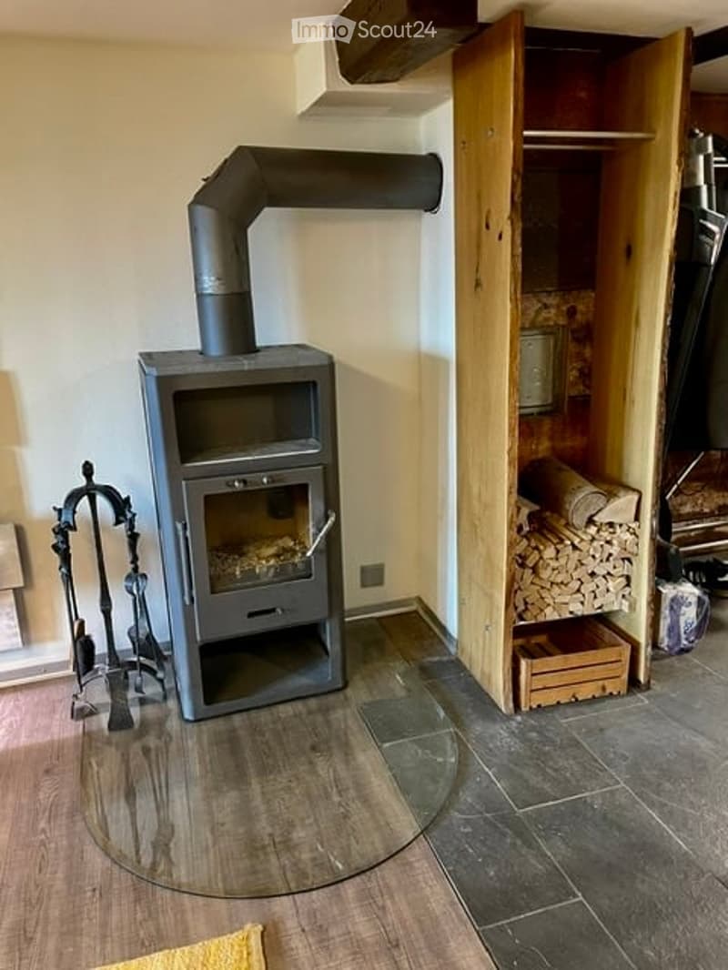 A cozy room with a wood stove, fireplace tools, and a wood storage cabinet with a stack of firewood.