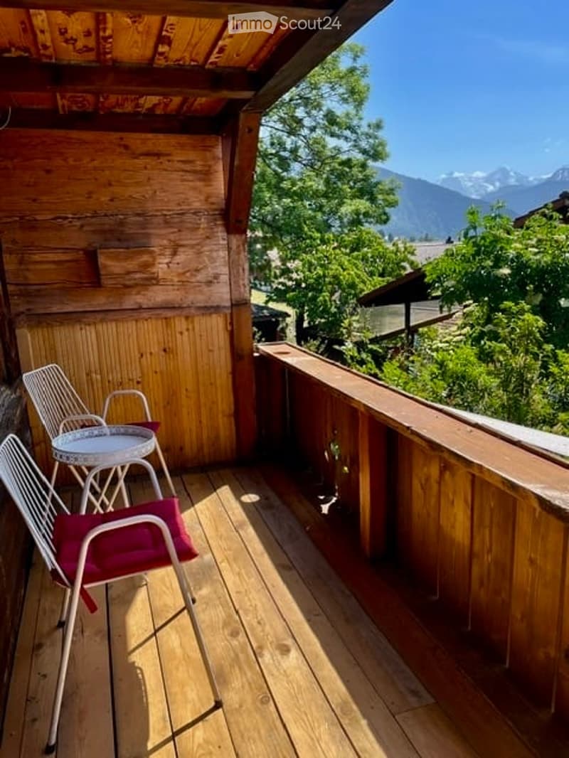 Wooden balcony with a view of mountains, featuring a small round table and two chairs.