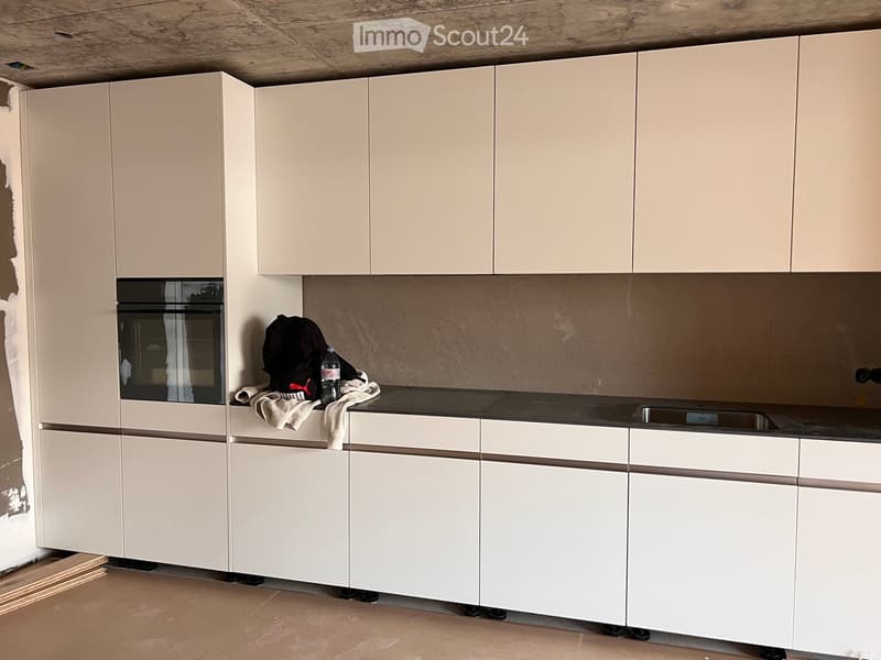 Modern kitchen with white cabinets, a built-in oven, and a countertop with a sink. A black backpack and a water bottle are placed on the counter.