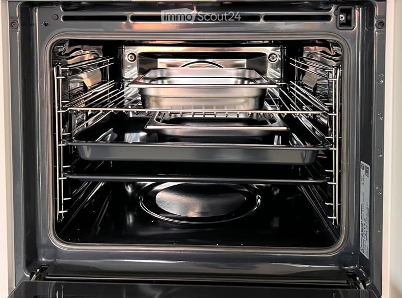 Open stainless steel oven with multiple racks and baking trays inside, clean and modern design.