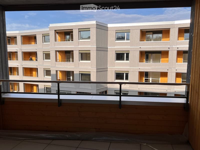 Balcony overlooking a modern multi-story residential building with grey and light wood facade, large windows, and balconies.