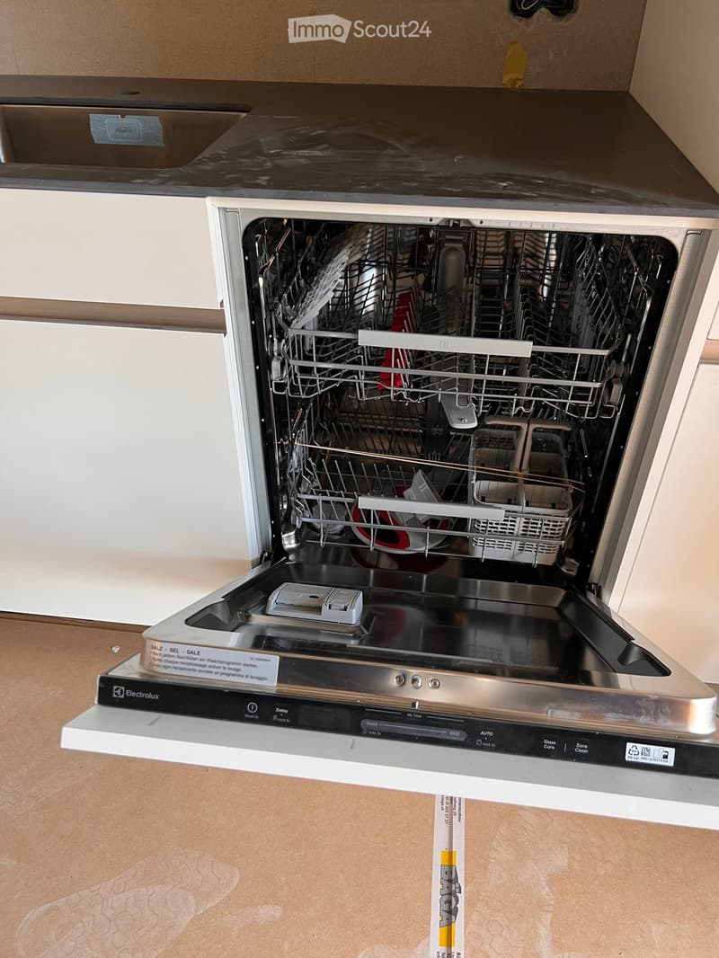 Open stainless steel dishwasher with multiple racks and cutlery inside, mounted under a dark countertop.