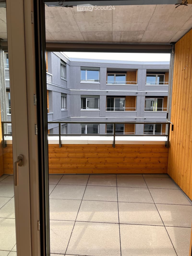 Balcony with tiled floor, wooden paneling, metal railing, and view of a modern building with multiple windows and balconies.