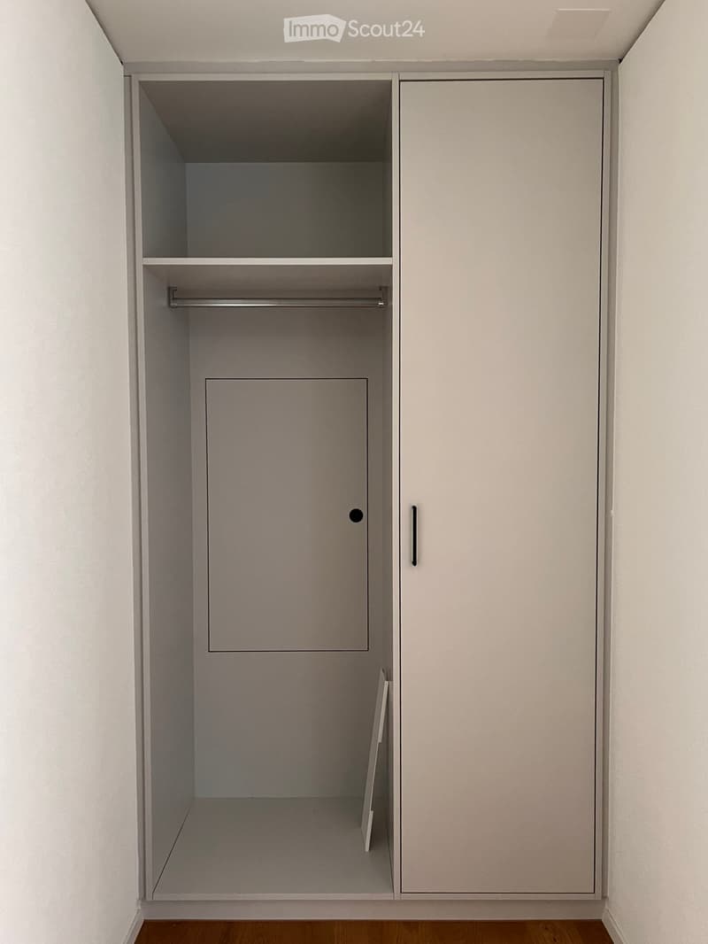 Empty closet with built-in shelves and a hanging rod, featuring light grey cabinetry and a wooden floor.