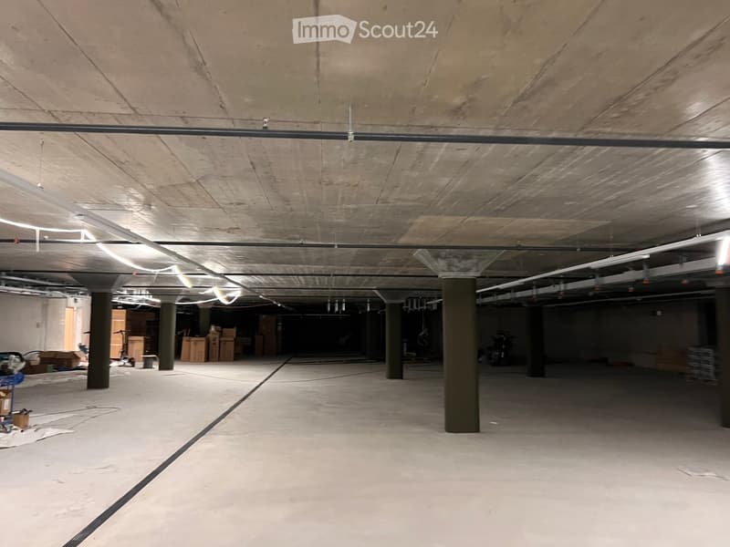 Empty underground parking area with concrete floors, exposed ceiling beams, and support pillars. No furniture or equipment present.