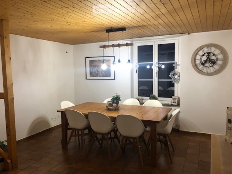 Dining room with wooden table, white chairs, pendant light fixture, picture frame on wall, and decorative clock.