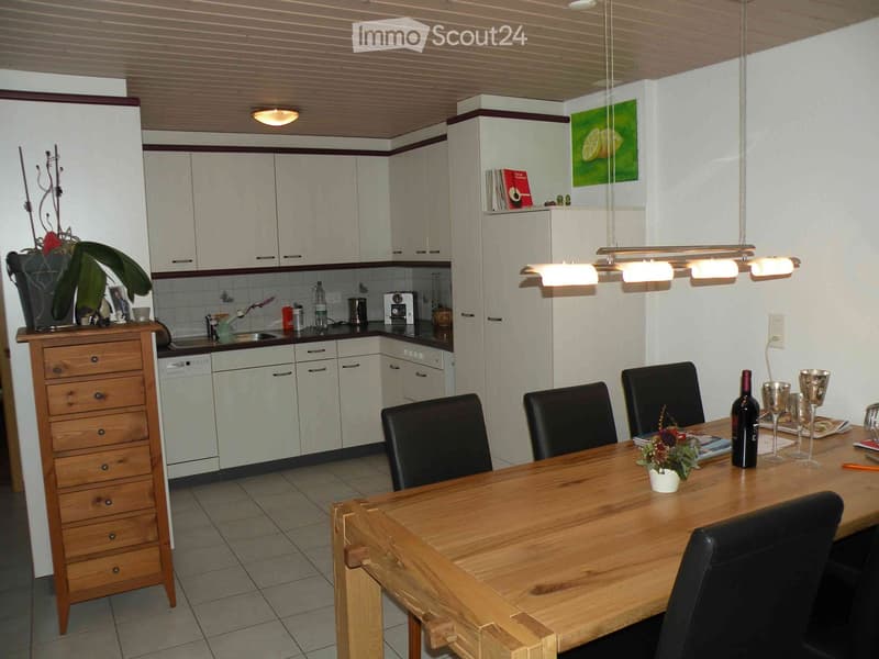 Modern kitchen with white cabinets, a wooden dining table with black chairs, and various appliances including a dishwasher and sink.