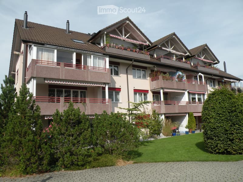 Multi-story residential building with balconies, large windows, and a well-maintained garden area.