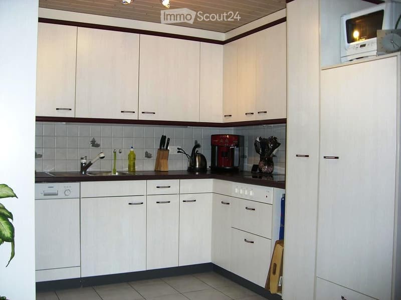 Modern kitchen with white cabinets, stainless steel appliances, and a dark countertop. Includes a sink, dishwasher, refrigerator, microwave, coffee maker, knife block, and decorative vase.