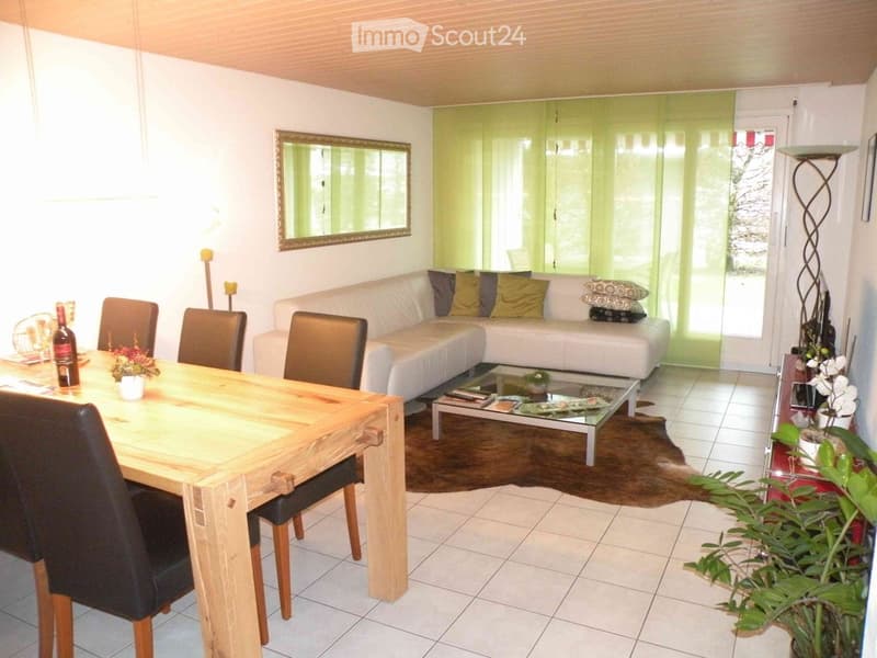 Bright living and dining area with a white sofa, coffee table, dining table with chairs, and a large mirror on the wall.