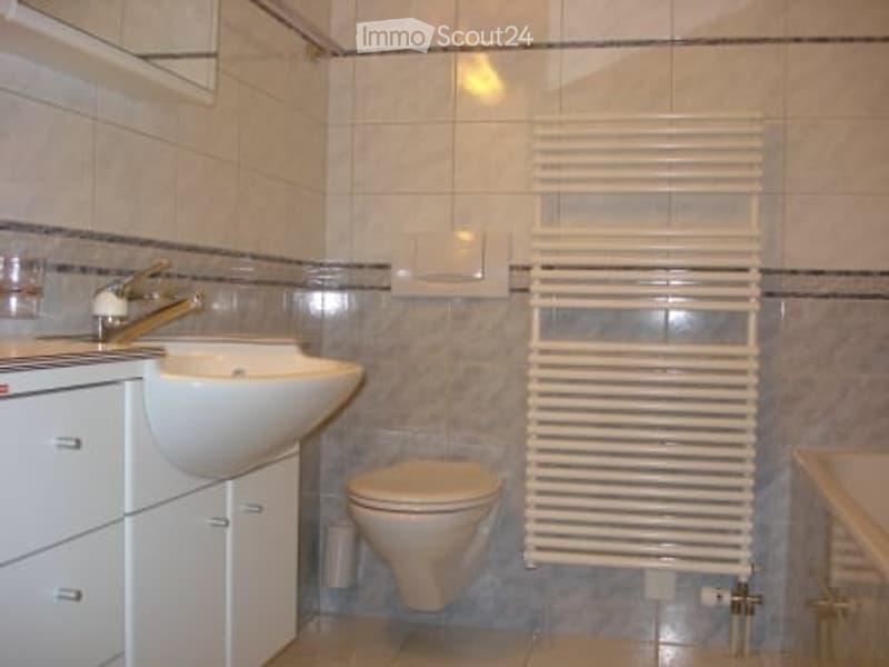Bathroom with white tiles, a sink with a faucet, a toilet, a radiator, and a cabinet.