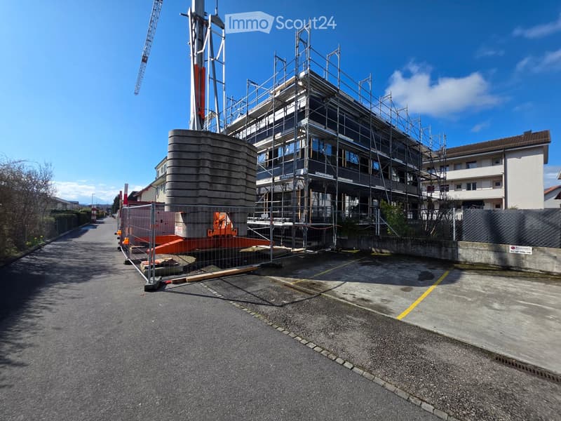 A multi-story building under construction with scaffolding, surrounded by a fenced area and construction materials.