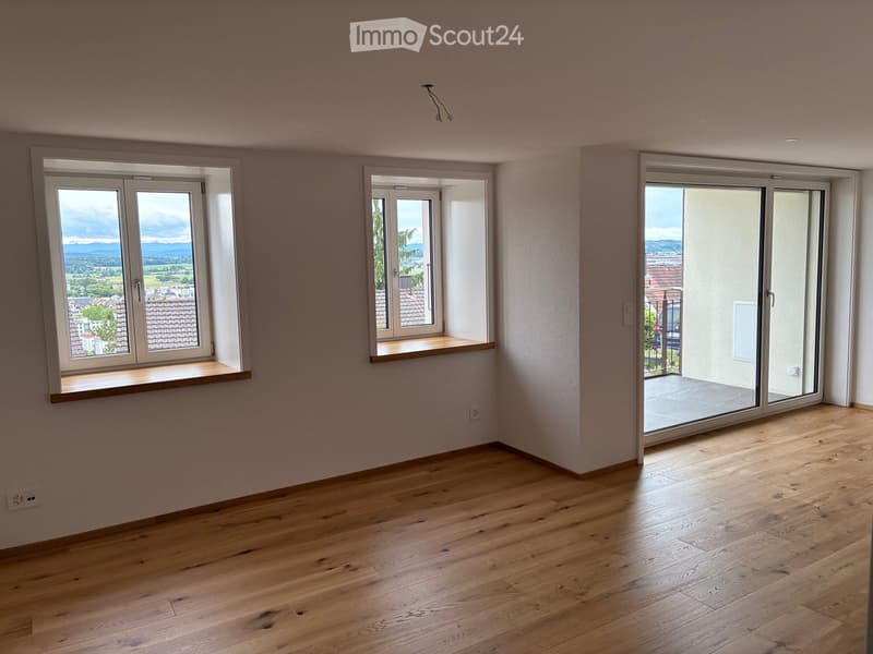 Empty room with wooden flooring, three windows, and a sliding door leading to a balcony.