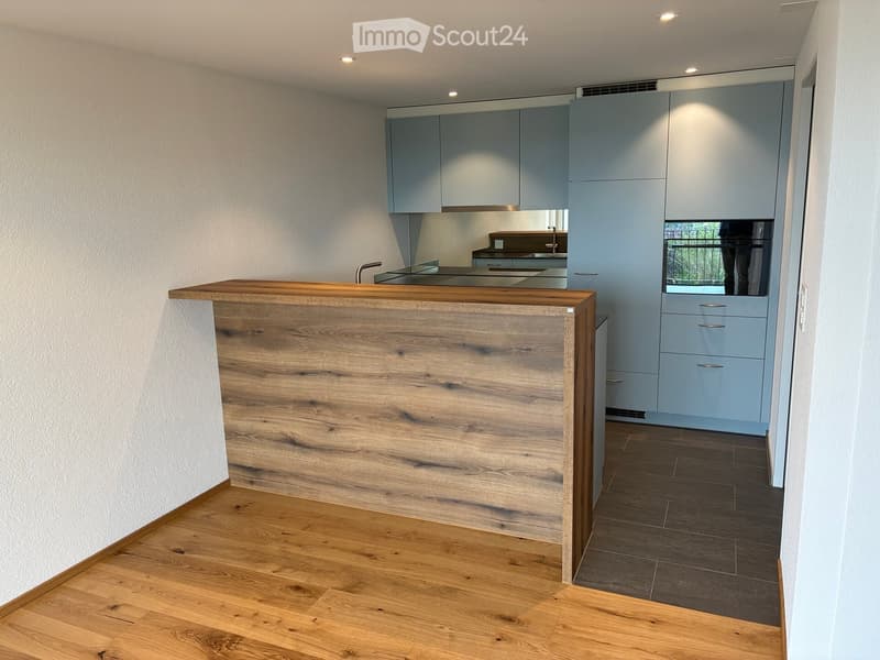 Modern kitchen with light blue cabinets, wooden counter, and dark tiled floor.