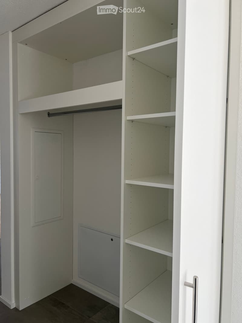 Empty closet with white shelves and a hanging rod, featuring a tiled floor and white walls.