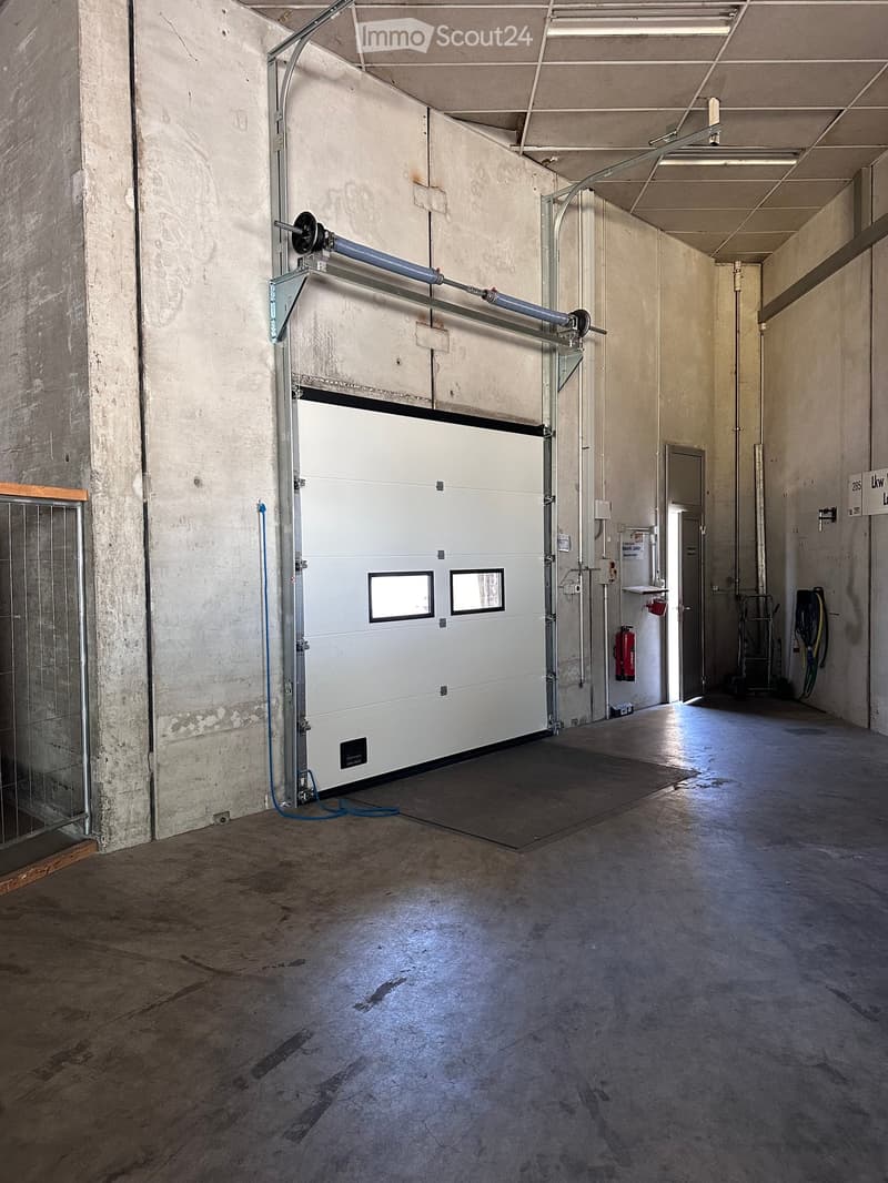 Empty industrial-style garage with a large white garage door, concrete floor, and minimal equipment.
