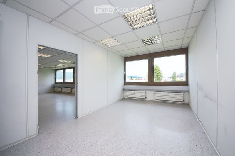 Empty room with white walls, a large window with a view, and a radiator below it. The room has a smooth, light-colored floor and a ceiling with recessed lighting.