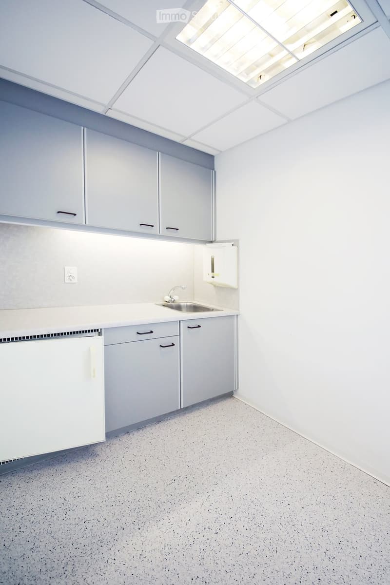 Empty kitchen with white cabinets, a sink, and a refrigerator, featuring a speckled concrete floor and a skylight above.