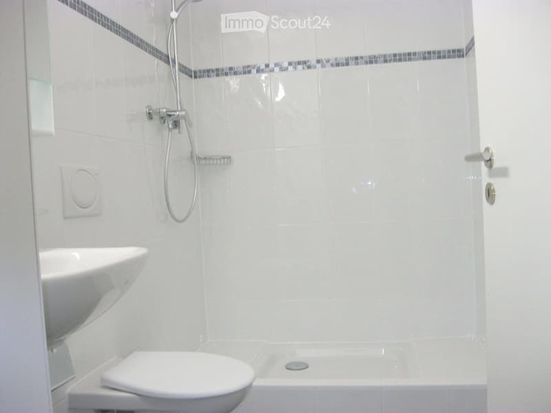 Modern bathroom with white tiles, a bathtub, toilet, sink, and a showerhead with a handheld hose.