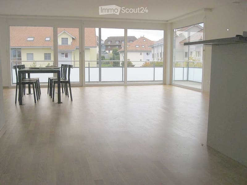 Bright, open room with wooden flooring, large windows, and a dining area with a table and chairs. The room has access to a balcony or terrace.