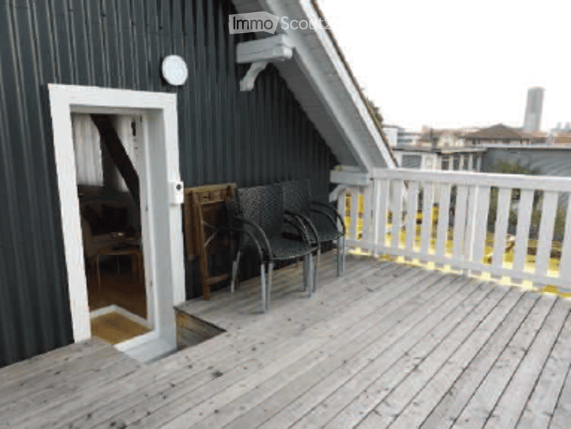 Wooden deck with white railing, two black chairs, and a small table, leading to an interior space.
