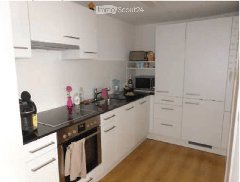 Modern kitchen with white cabinets, black countertops, and wooden flooring. Features an oven, microwave, and various kitchen items.