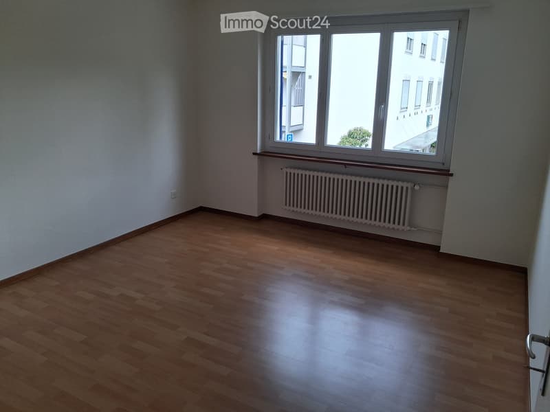 Empty room with wooden flooring, white walls, and a large window with a radiator below it.