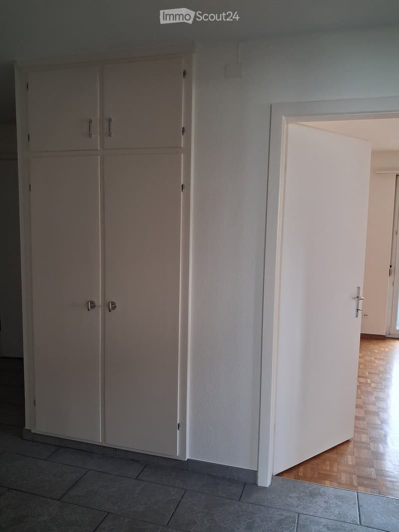 Empty hallway with tiled floor, white walls, and a wooden door leading to another room.