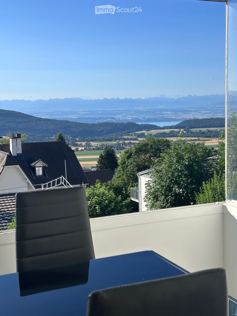 Balcony with a scenic mountain view, featuring a black leather chair and a blue table.