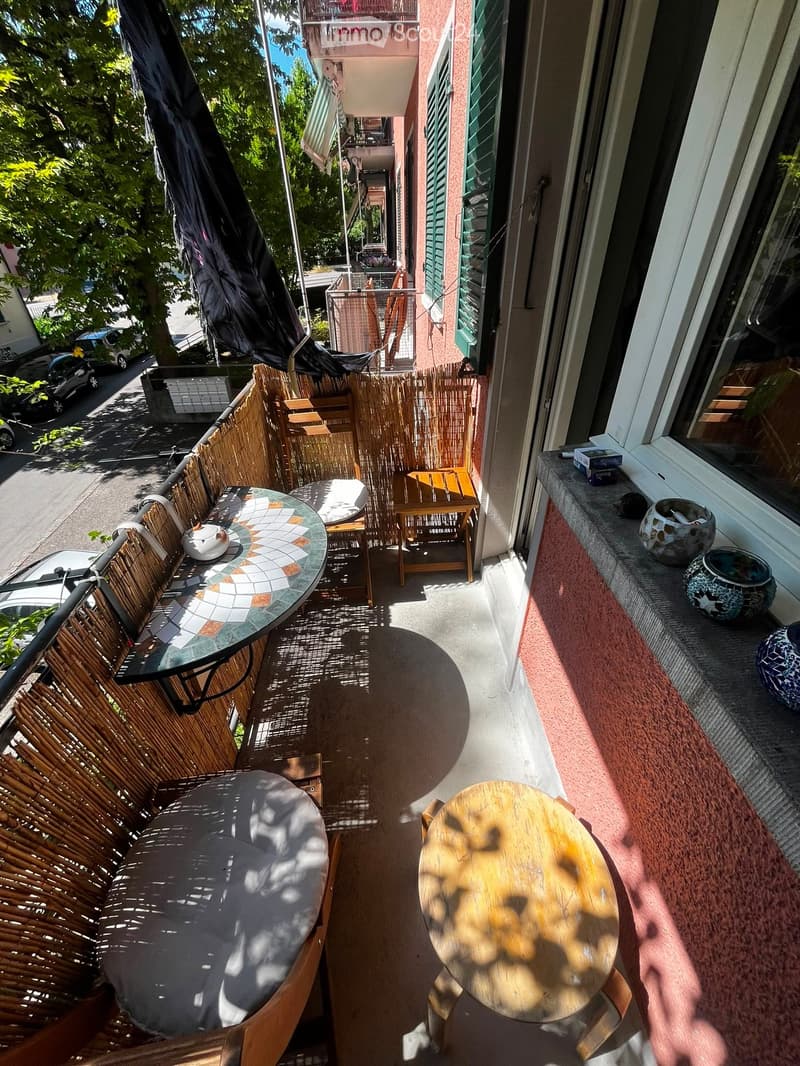 Balcony with a round glass table, wicker chairs, a small wooden stool, and decorative vases on the windowsill.