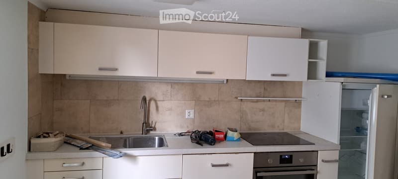 Modern kitchen with white cabinets, stainless steel sink, and built-in appliances. Countertop has various items including a camera and tools.
