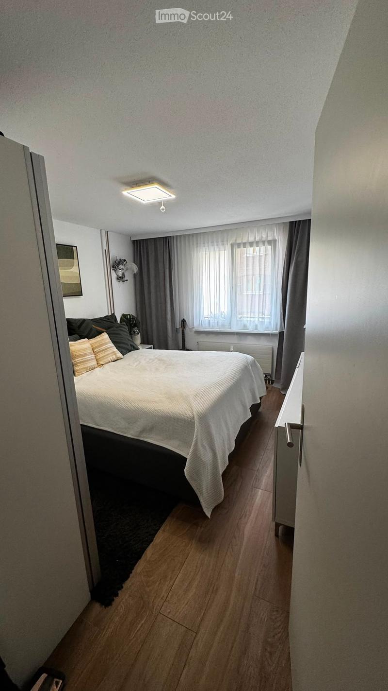 Cozy bedroom with a double bed, pillows, nightstand, guitar, and a window with curtains. Wooden flooring and modern lighting.