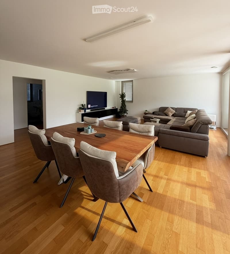 Modern living and dining area with hardwood flooring, a large sectional sofa, a coffee table, an ottoman, a dining table with six chairs, and a television on a stand.
