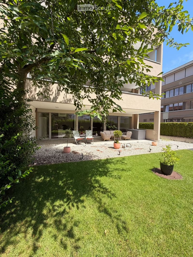 Well-maintained garden with a lawn, gravel area, potted plants, and outdoor seating including chairs and a sofa.