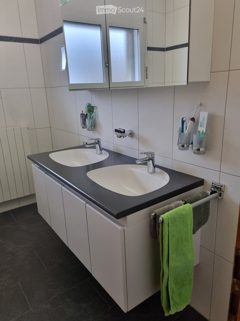 Bathroom with double sink, white cabinets, tiled walls, towel rack, and a mirror.