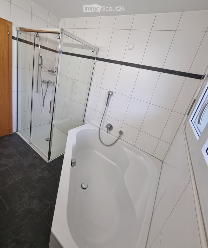 Bathroom with white tiles, bathtub, shower, and wooden door.
