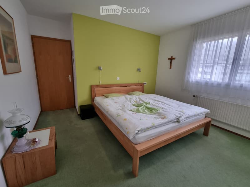 bedroom with bed, nightstand, lamp, radiator, picture, door, cross, window