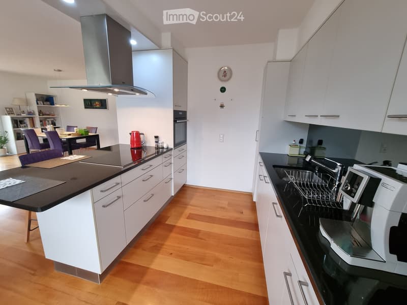 modern kitchen with white cabinets, black countertops, stainless steel appliances, wooden floor, open to dining area