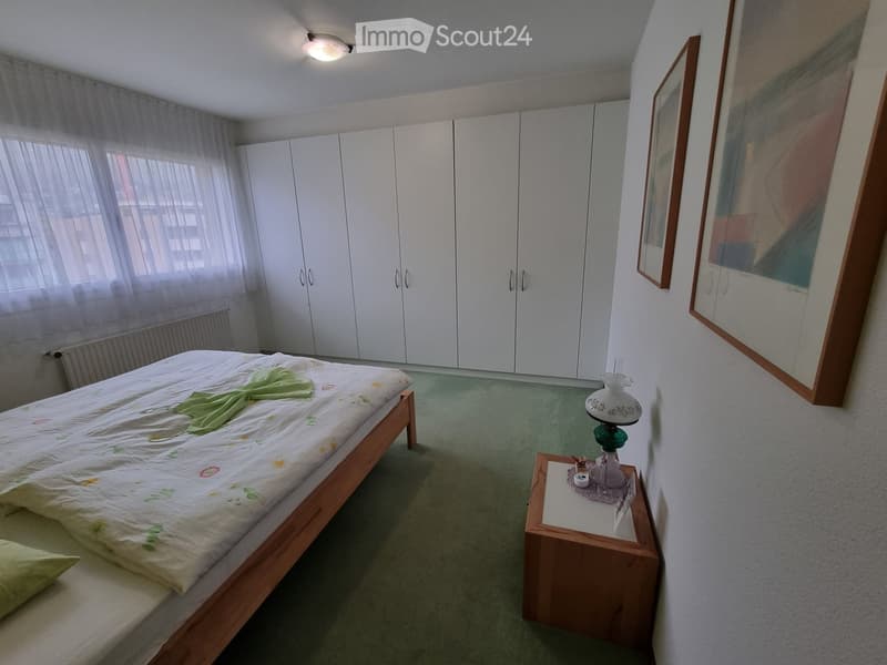 Bedroom with a bed, white wardrobes, a nightstand, a radiator, and two paintings on the wall.