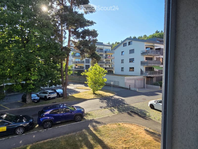 View of a modern residential complex with multiple buildings, balconies, and parked cars in a sunny outdoor setting.