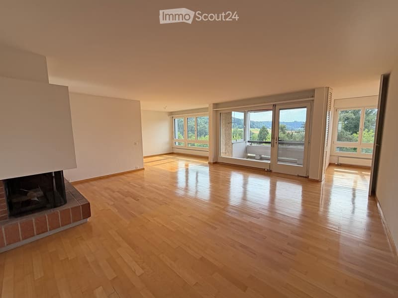 Empty room with wooden flooring, fireplace, large windows, and sliding glass doors leading to a balcony with scenic views.