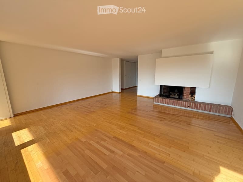 Empty room with wooden flooring, white walls, and a fireplace with a brick surround.