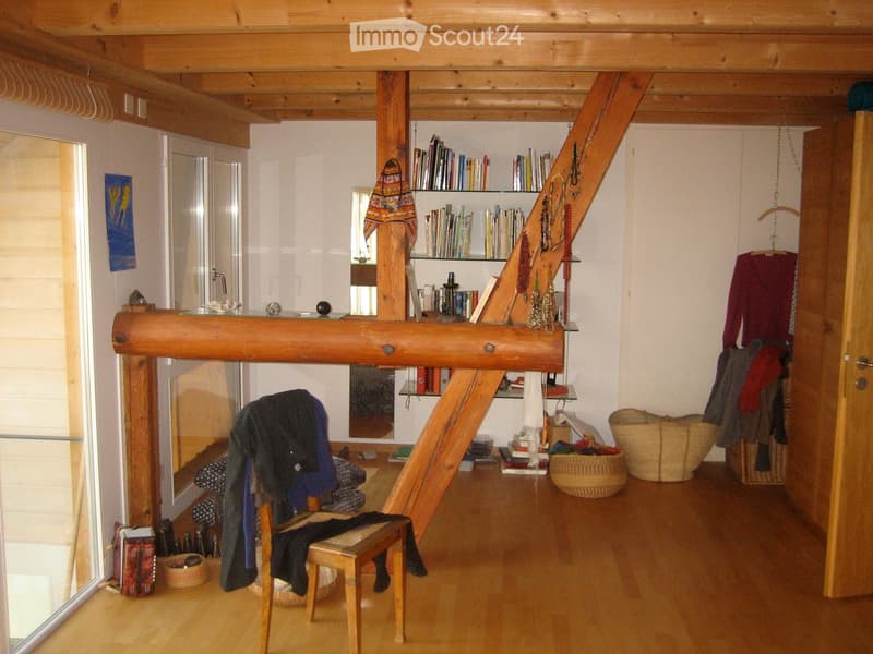 A cozy, wooden-framed room with a chair draped with clothes, a bookshelf filled with books, and several baskets on the floor.