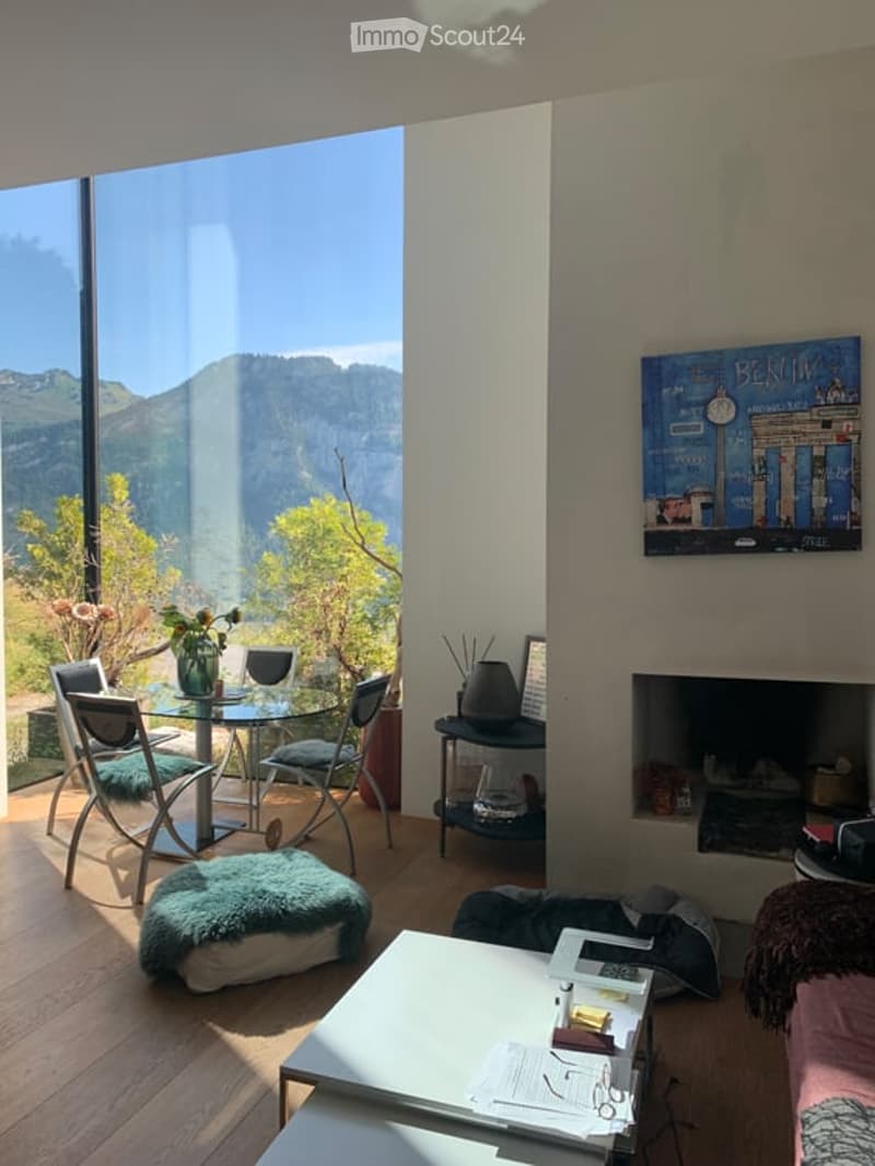 Bright living room with large windows offering a scenic mountain view. Features a fireplace, a coffee table, a sofa, a dining table with chairs, and decorative items including a vase and picture frame.