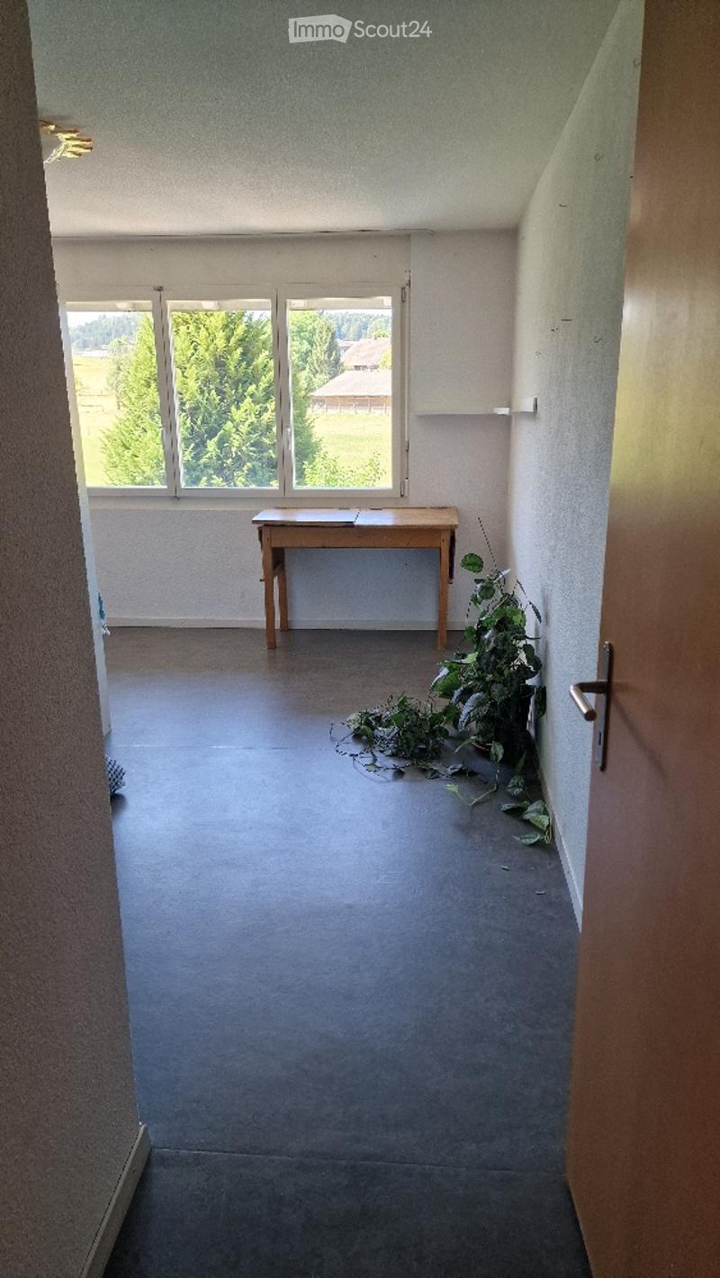 Empty room with bare walls, wooden floor, and a small wooden table near the window. No furniture or equipment.