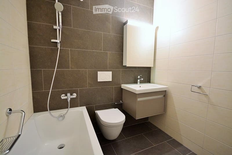 Modern bathroom with a bathtub, toilet, sink, and showerhead. Features tiled walls and a built-in cabinet.