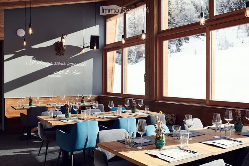 A cozy restaurant interior with wooden tables, blue chairs, wine glasses, and decorative vases. Large windows offer a view of a snowy landscape.
