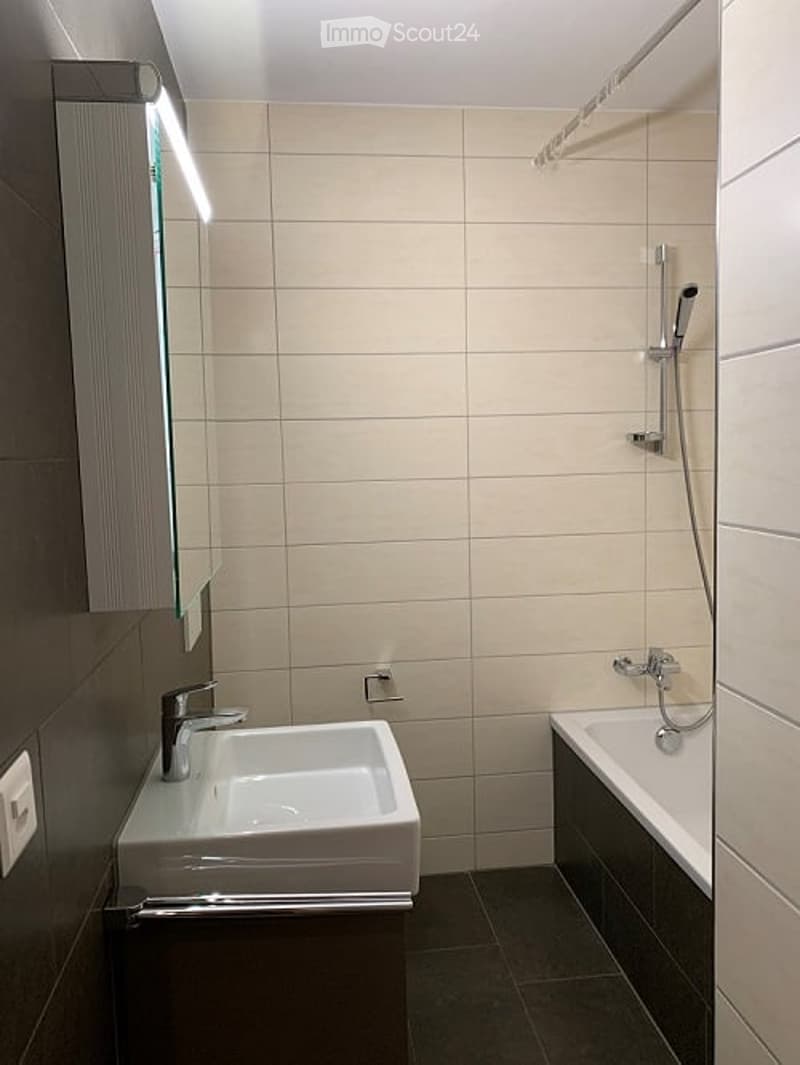 Bathroom with white sink, bathtub, shower, mirror, and tiled walls