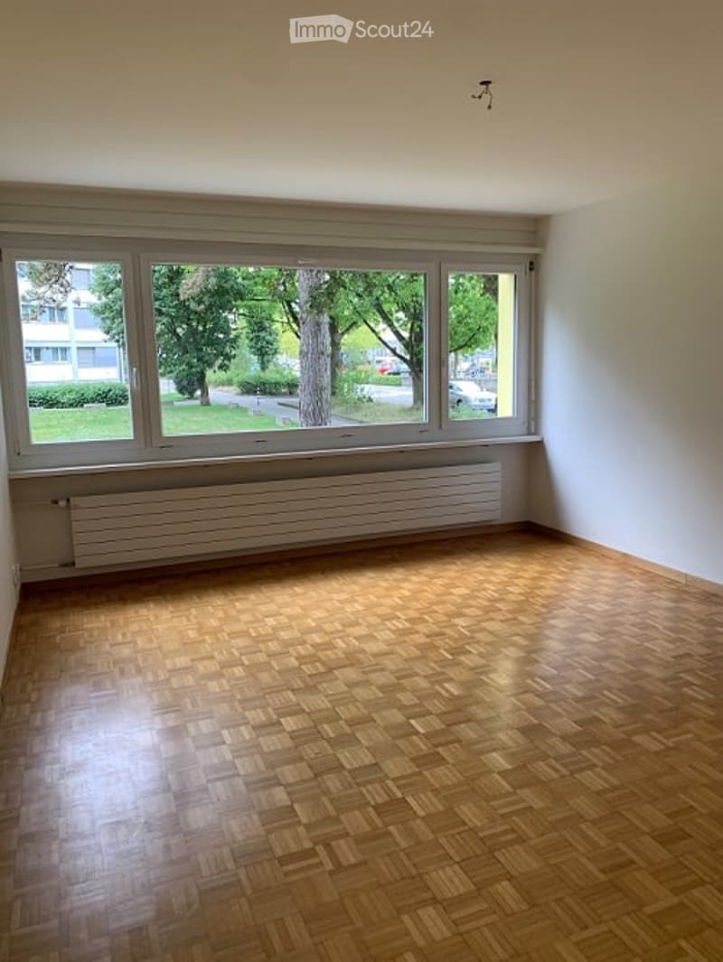 Empty room with wooden floor, large windows, white walls, and a view of the outside