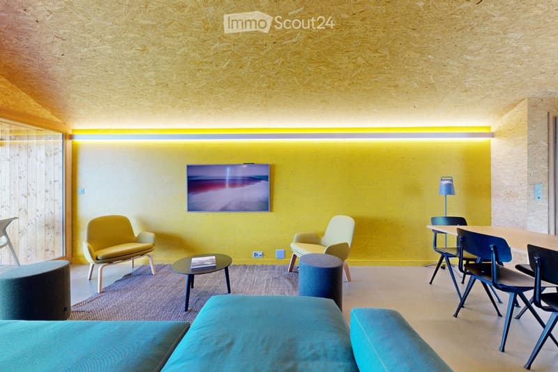 Modern living room with yellow accent wall, blue sofa, yellow chairs, round coffee table, and a screen mounted on the wall.